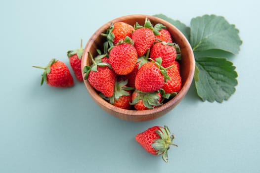 A bowl of beautiful and delicious strawberries isolated on a blue-green background, closeup, topview, copyspace.