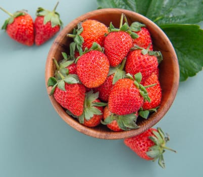 A bowl of beautiful and delicious strawberries isolated on a blue-green background, closeup, topview, copyspace.