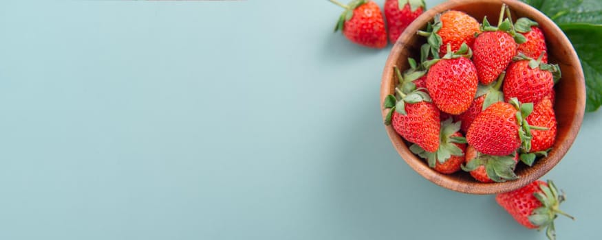A bowl of beautiful and delicious strawberries isolated on a blue-green background, closeup, topview, copyspace.