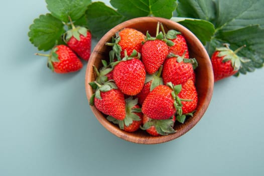A bowl of beautiful and delicious strawberries isolated on a blue-green background, closeup, topview, copyspace.