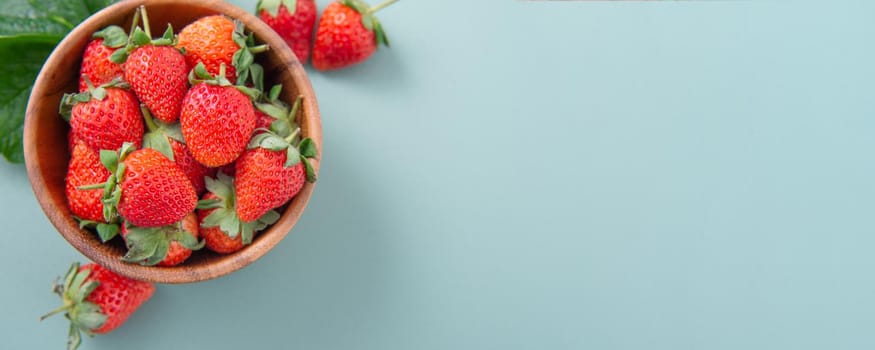 A bowl of beautiful and delicious strawberries isolated on a blue-green background, closeup, topview, copyspace.