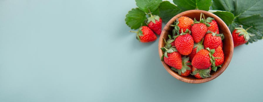 A bowl of beautiful and delicious strawberries isolated on a blue-green background, closeup, topview, copyspace.