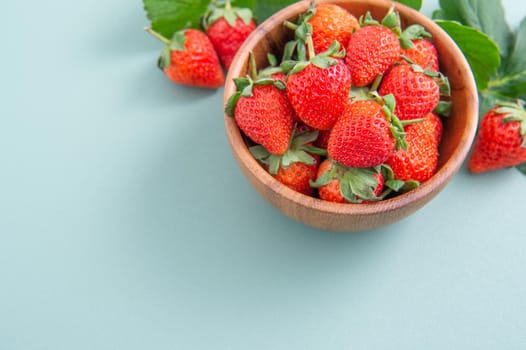 A bowl of beautiful and delicious strawberries isolated on a blue-green background, closeup, topview, copyspace.