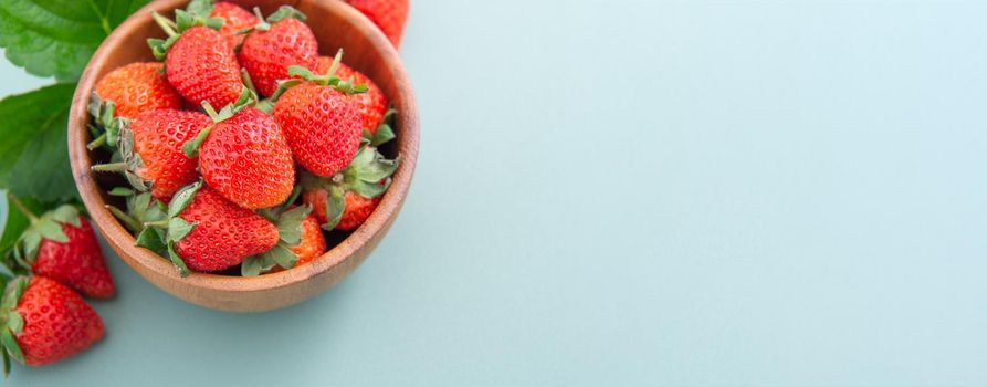 A bowl of beautiful and delicious strawberries isolated on a blue-green background, closeup, topview, copyspace.