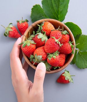 A young woman is holding a bowl of strawberries isolated on a airy blue background, closeup, topview, copyspace.