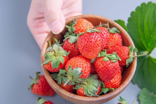 A young woman is holding a bowl of strawberries isolated on a airy blue background, closeup, topview, copyspace.