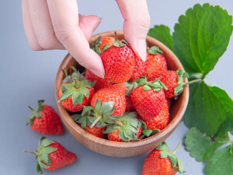 A young woman is holding a bowl of strawberries isolated on a airy blue background, closeup, topview, copyspace.