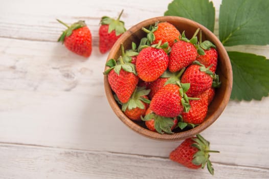 A bowl of beautiful and delicious strawberries isolated on a light wooden background, closeup, topview, copyspace.