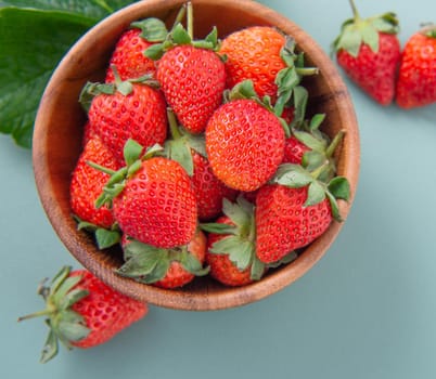 A bowl of beautiful and delicious strawberries isolated on a blue-green background, closeup, topview, copyspace.