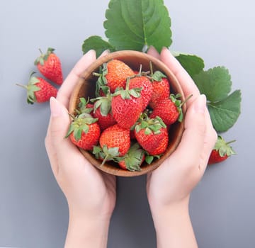 A young woman is holding a bowl of strawberries isolated on a airy blue background, closeup, topview, copyspace.
