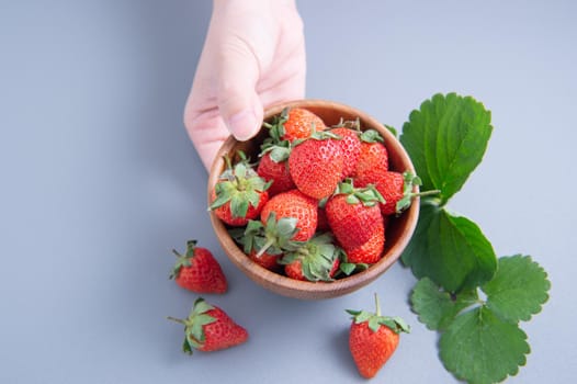 A young woman is holding a bowl of strawberries isolated on a airy blue background, closeup, topview, copyspace.