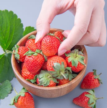A young woman is holding a bowl of strawberries isolated on a airy blue background, closeup, topview, copyspace.
