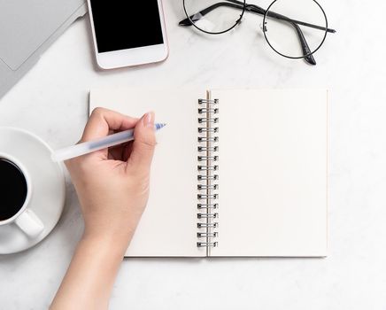 A woman is writing notes isolated on stylized marble office working desk with smartphone, laptop, glasses and coffee, mock up, topview, flatlay, copyspace, closeup