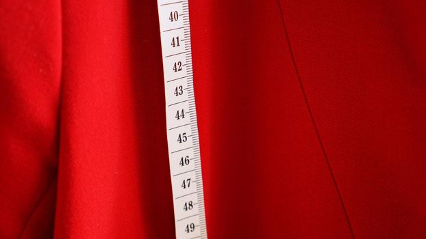 White measuring tape on the background of the red fabric of the jacket. Sewing clothes concept