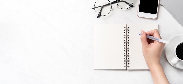 A woman is writing notes isolated on stylized marble office working desk with smartphone, laptop, glasses and coffee, mock up, topview, flatlay, copyspace, closeup