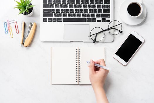 A woman is writing notes isolated on stylized marble office working desk with smartphone, laptop, glasses and coffee, mock up, topview, flatlay, copyspace, closeup