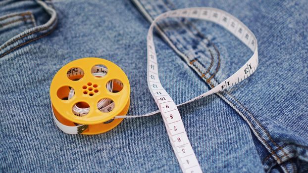 Blue jeans and a measuring tape. Slimming or sewing denim concept. Measuring tape in yellow spool on denim background