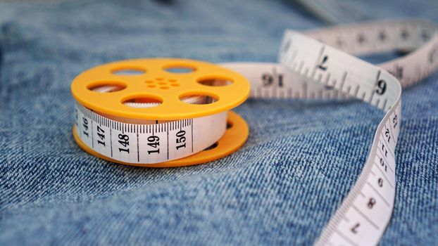 Blue jeans and a measuring tape. Slimming or sewing denim concept. Measuring tape in yellow spool on denim background