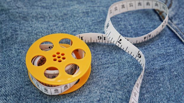 Blue jeans and a measuring tape. Slimming or sewing denim concept. Measuring tape in yellow spool on denim background