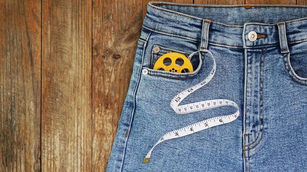 Blue jeans and a measuring tape. Slimming or sewing denim concept. Jeans on wooden background