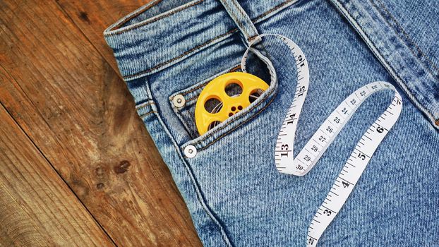 Blue jeans and a measuring tape. Slimming or sewing denim concept. Jeans on wooden background