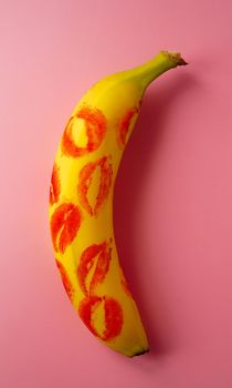 Red lipstick on a yellow banana on a pink background. Love and sex concept.