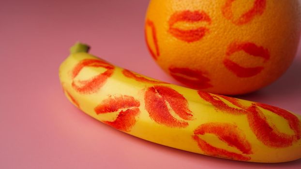 Composition with fresh banana with traces of red lipstick and grapefruit on pink background. Sex concept