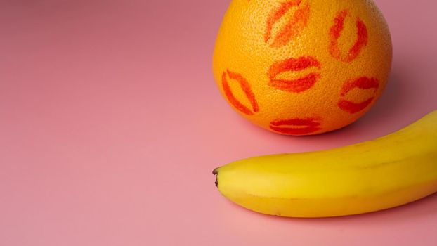 Composition with fresh banana with traces of red lipstick and grapefruit on pink background. Sex concept