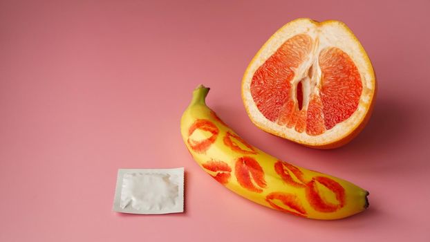 Banana with traces of red lipstick and grapefruit with condom on pink background. Safe Sex Concept