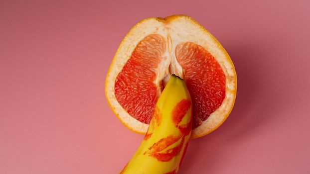Composition with fresh banana with traces of red lipstick and grapefruit on pink background. Sex concept