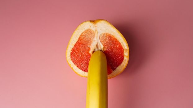 Banana with red grapefruit on pink background, sex concept