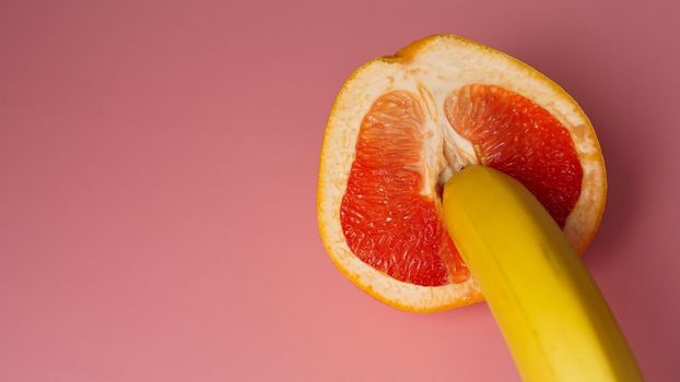 Banana with red grapefruit on pink background, sex concept