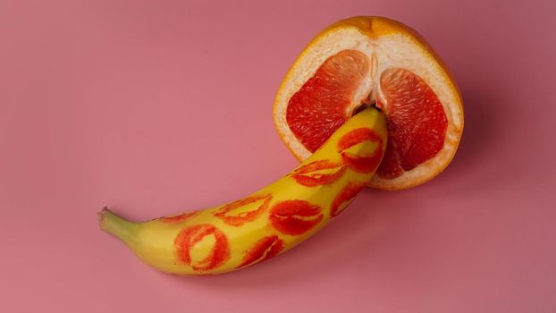 Composition with fresh banana with traces of red lipstick and grapefruit on pink background. Sex concept