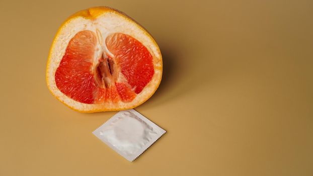 Fresh grapefruit and white condom on golden color background
