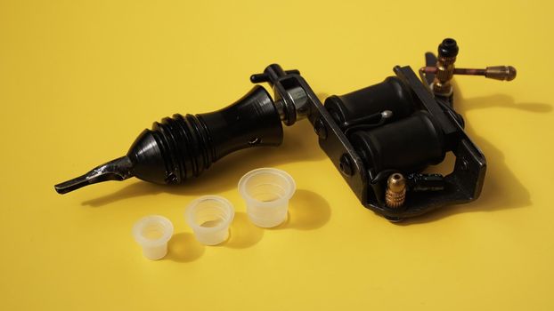 Tattoo equipment, tattoo ink plastic caps and tattoo machine on yellow background