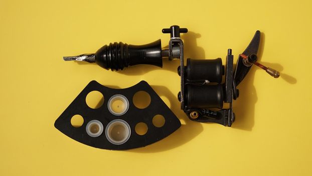 Tattoo equipment, tattoo ink plastic caps and tattoo machine on yellow background