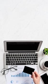 A woman is doing a online payment or shopping, mock up credit card and mobile phone on office desk isolated on beautiful fashion marble background, topview, flatlay, copyspace.