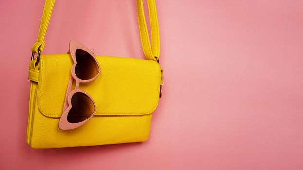Yellow bag and heart-shaped sunglasses on pink background - summer picture