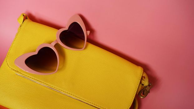 Yellow bag and heart-shaped sunglasses on pink background - summer picture