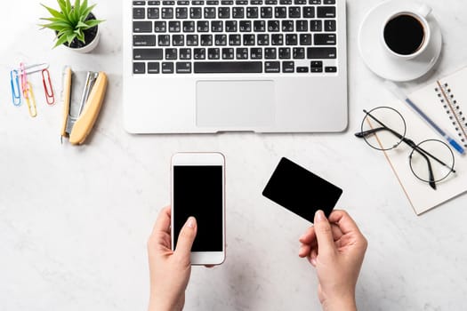 A woman is doing a online purchase, mock up credit card and mobile cellphone on office desk isolated on beautiful fashion marble background, copy space, topview, flatlay, closeup