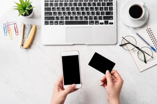 A woman is doing a online purchase, mock up credit card and mobile cellphone on office desk isolated on beautiful fashion marble background, copy space, topview, flatlay, closeup