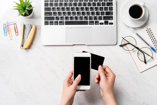 A woman is doing a online purchase, mock up credit card and mobile cellphone on office desk isolated on beautiful fashion marble background, copy space, topview, flatlay, closeup