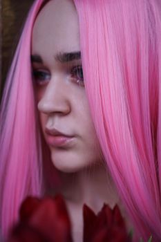 Close up fashion portrait. Vertical photo. Portrait of a dreamy girl with bright pink hair with flowers close to face. Looking to the side