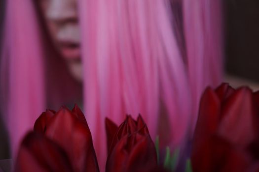 Out of focus, blurred background. Portrait of a dreamy girl with bright pink hair with flowers close to face. Looking to the side