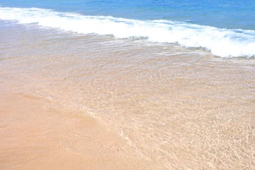 Beautiful amazing gold colored sandy beach with soft waves isolated with sunny blue sky. Concept of tropical calm tourism idea, copy space, close up