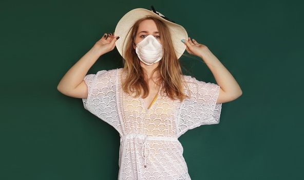 Beautiful girl in a white summer dress. Medical mask on the face. Closed borders during coronavirus. Tourist on a green background