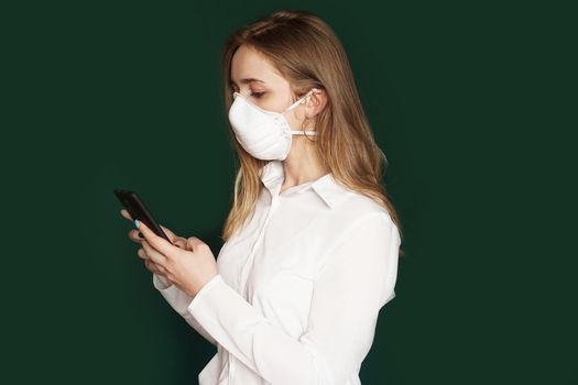 Girl in a medical mask, phone in hands, on a green background. COVID-19 outbreak of coronavirus. office concept