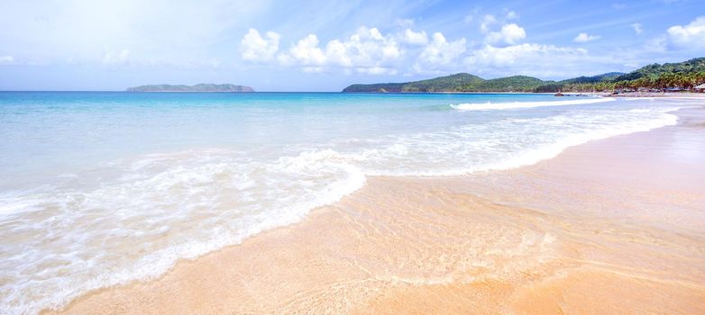 Beautiful amazing gold colored sandy beach with soft waves isolated with sunny blue sky. Concept of tropical calm tourism idea, copy space, close up