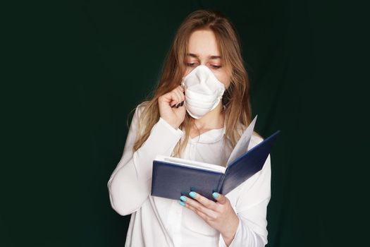 Young girl in a medical mask in a white office blouse with a notebook in hand on a green background