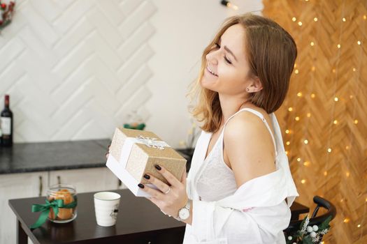 Beautiful girl dressed in a white shirt holding a gift in a modern bright kitchen